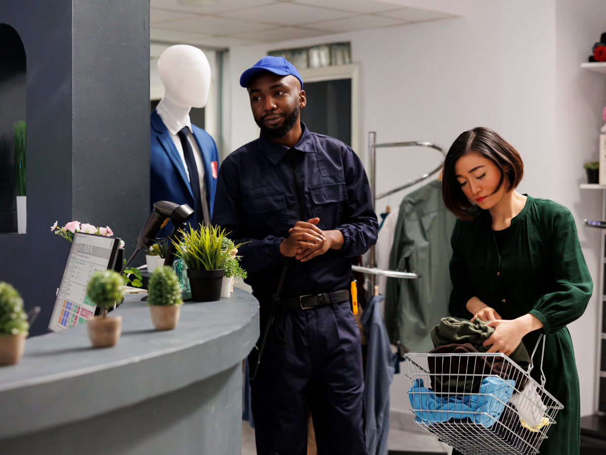Man in blue uniform looks towards woman sorting laundry at a shop counter.