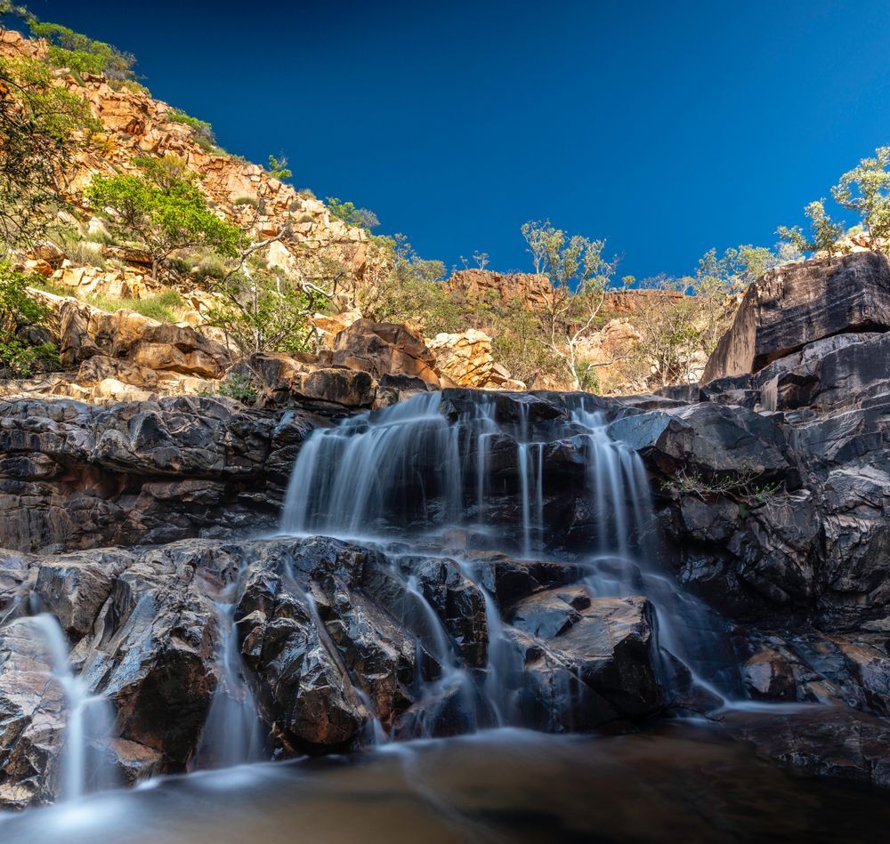 A Waterfall Surrounded by Rocks and Trees With a Blue Sky in the Background — Linmar Cranes & Haulage in Cloncurry, QLD