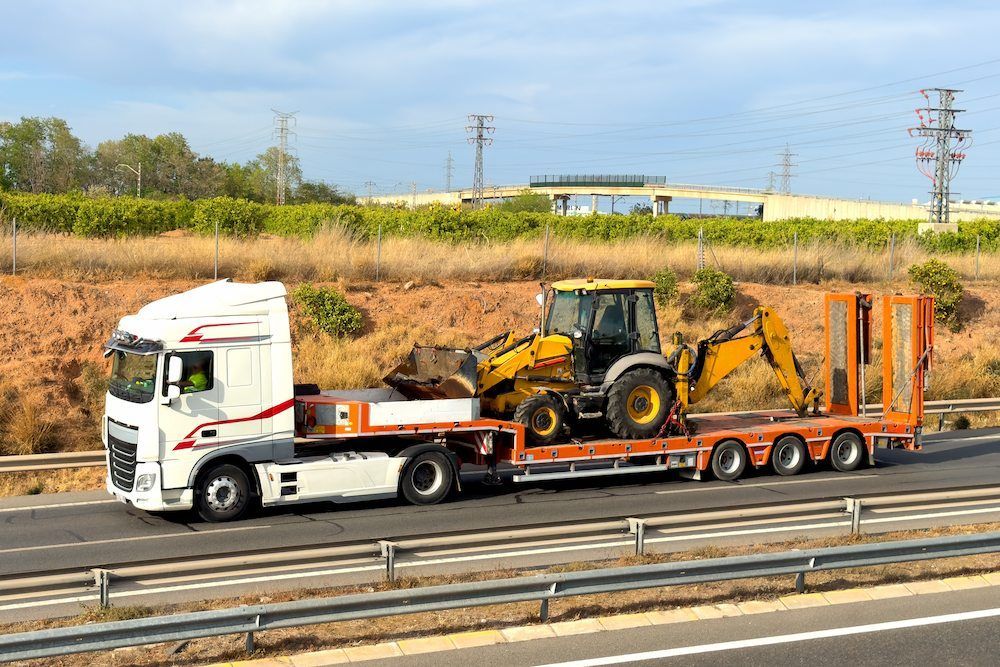 A Semi Truck Is Carrying a Tractor on A Trailer on A Highway — Linmar Cranes & Haulage in Northern Territory