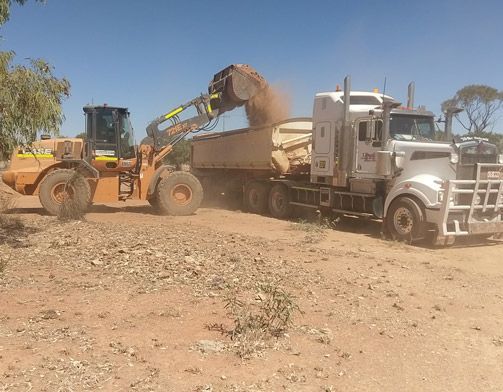 A Bulldozer is Loading Dirt Into a Dump Truck — Linmar Cranes & Haulage in Kalkadoon, QLD