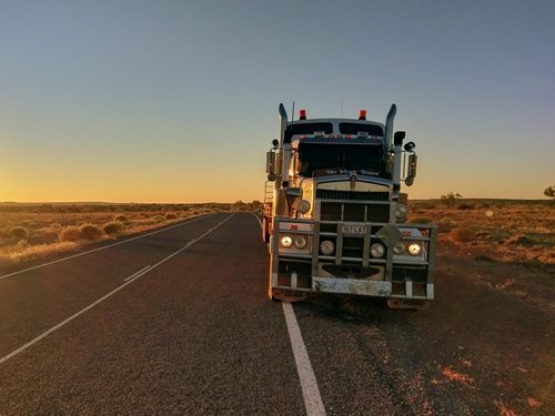 A Semi Truck is Driving Down a Desert Road at Sunset — Linmar Cranes & Haulage in Kalkadoon, QLD