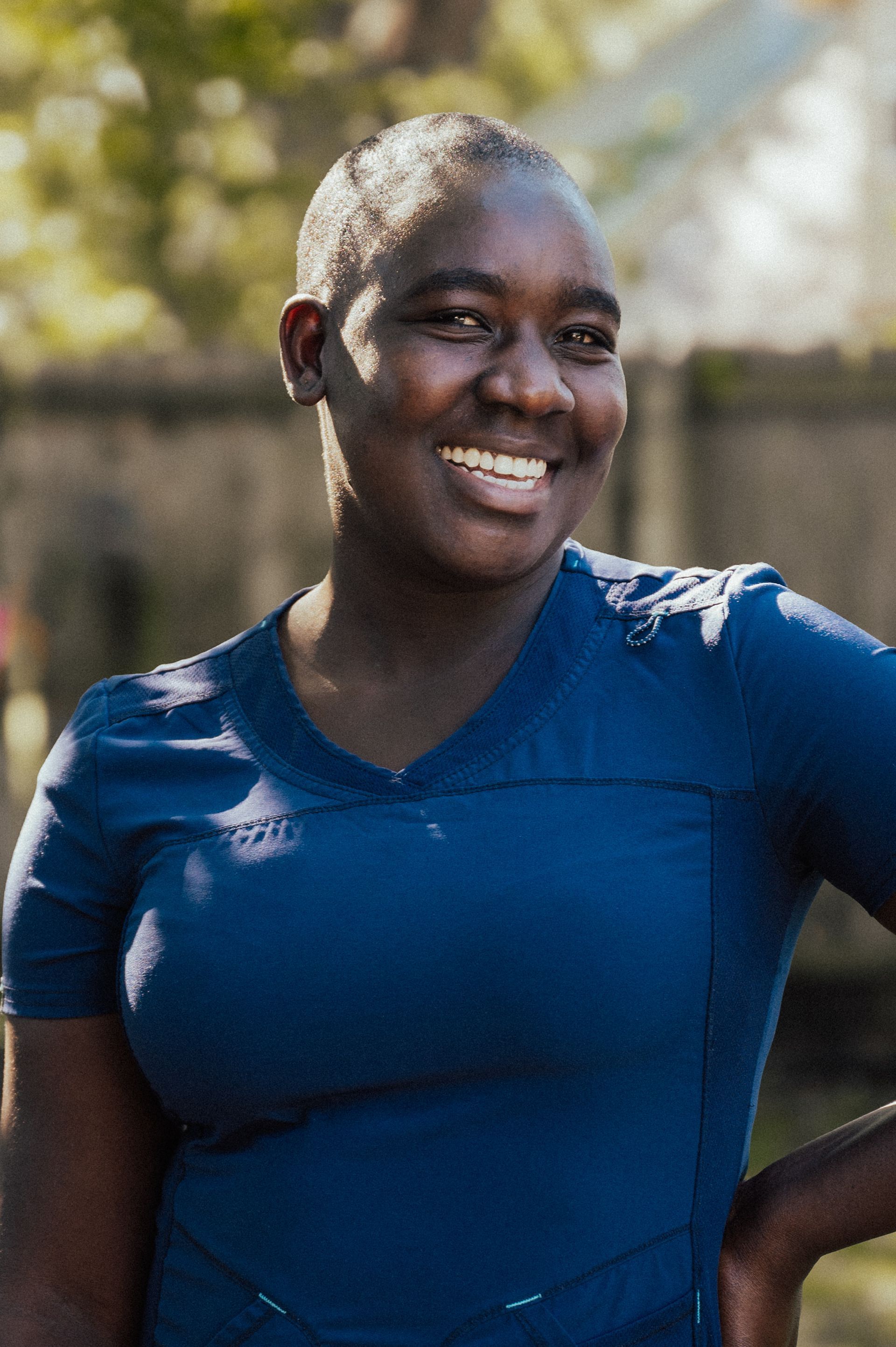 Smiling Black woman in blue scrubs outdoors.