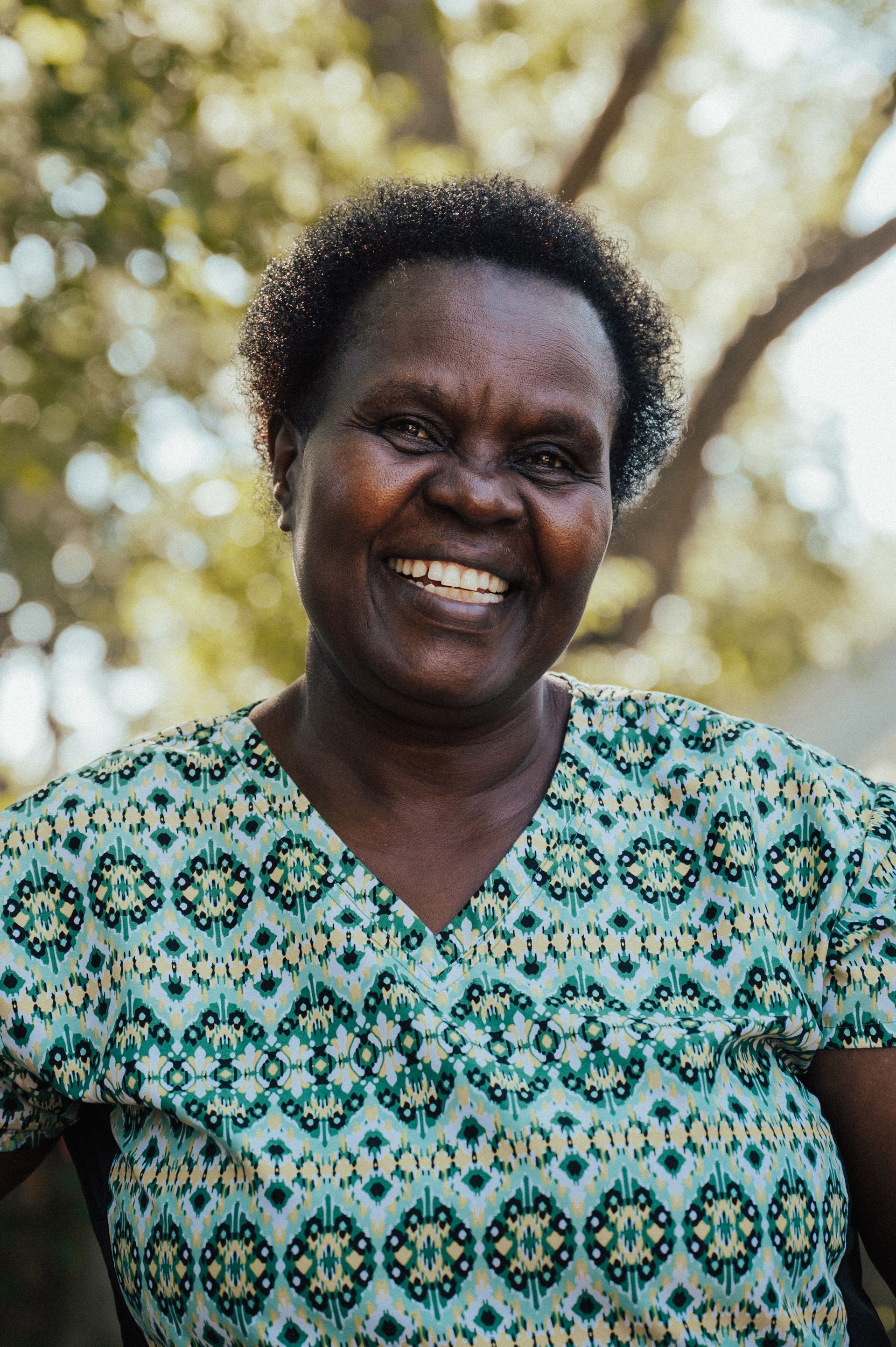 Woman smiles at camera, outdoors. She wears a patterned blue shirt.