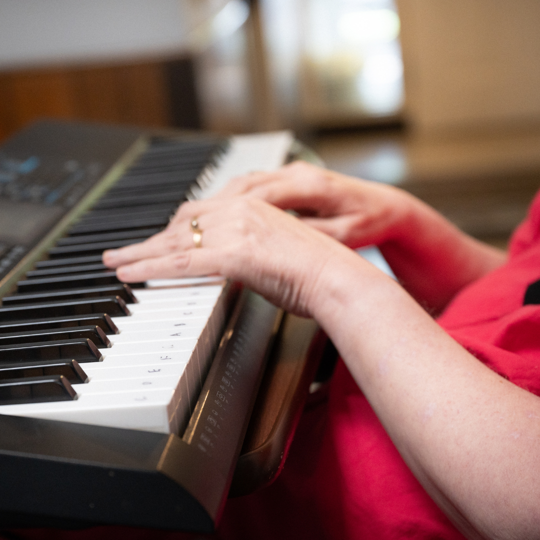 Close-up of a person's hands playing a black and white keyboard, wearing a red shirt.