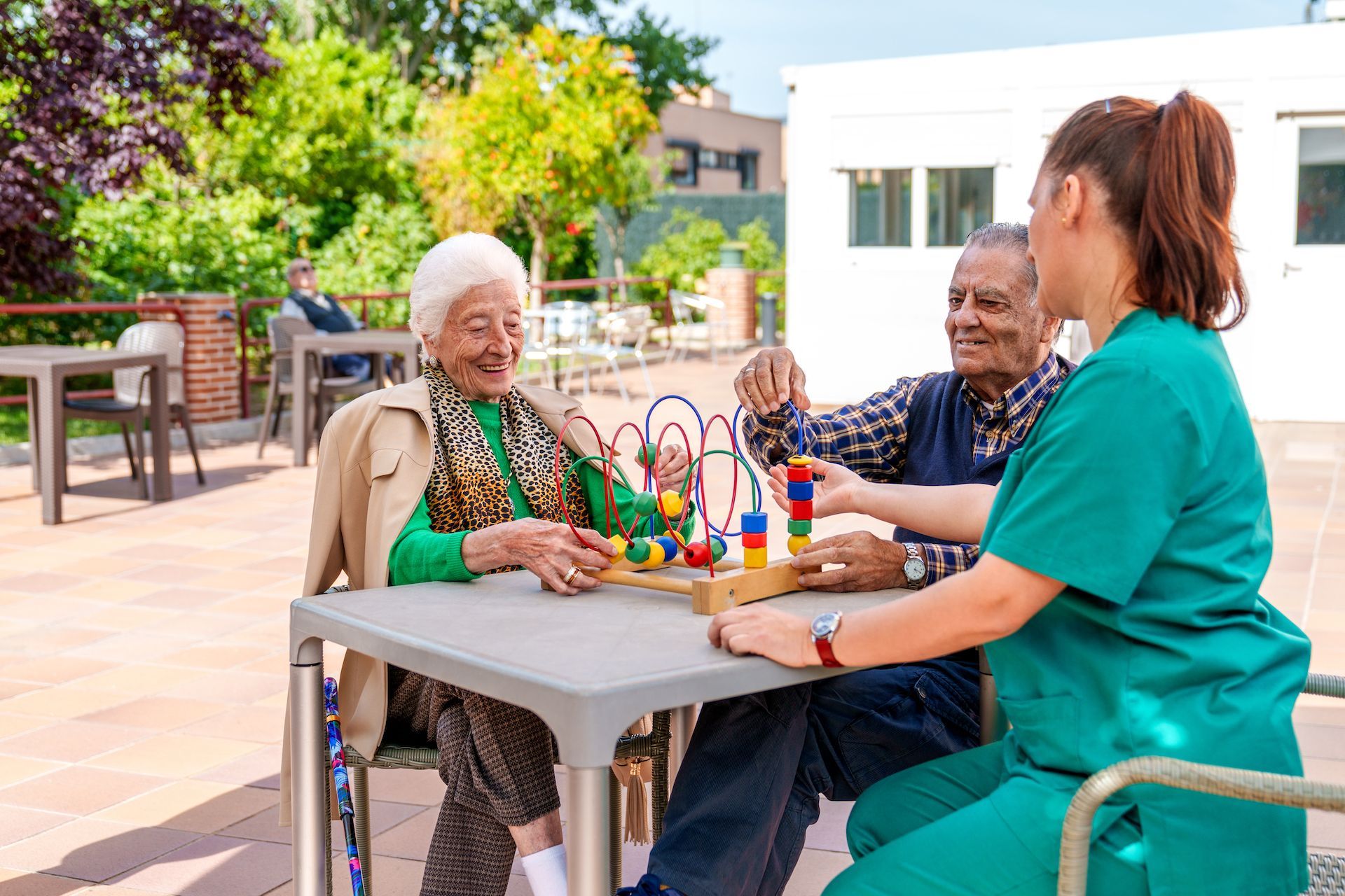 A group of elderly people are sitting at a table playing a game with a nurse.