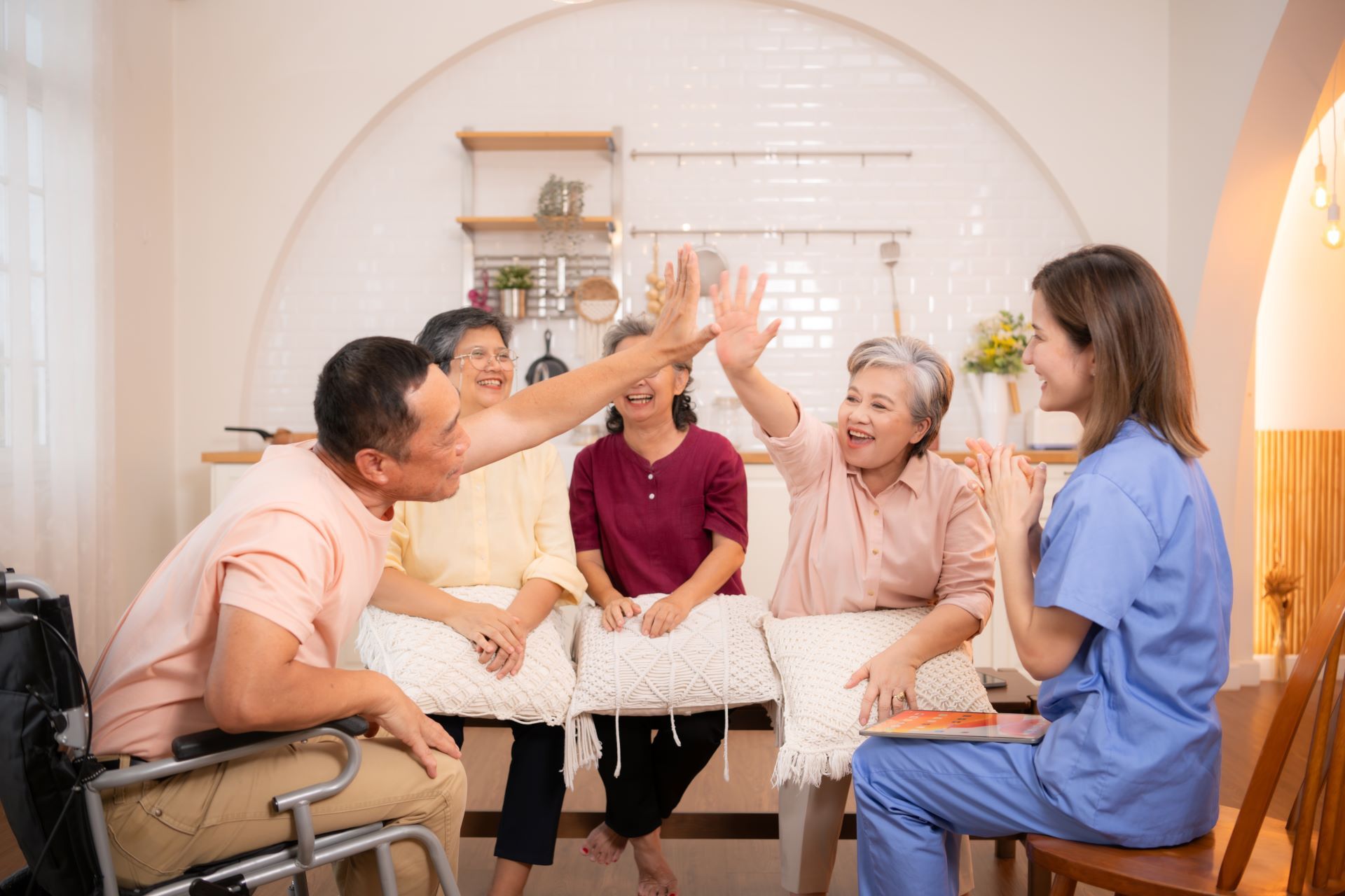 Group of older adults and a caregiver are celebrating with high fives in a kitchen setting.