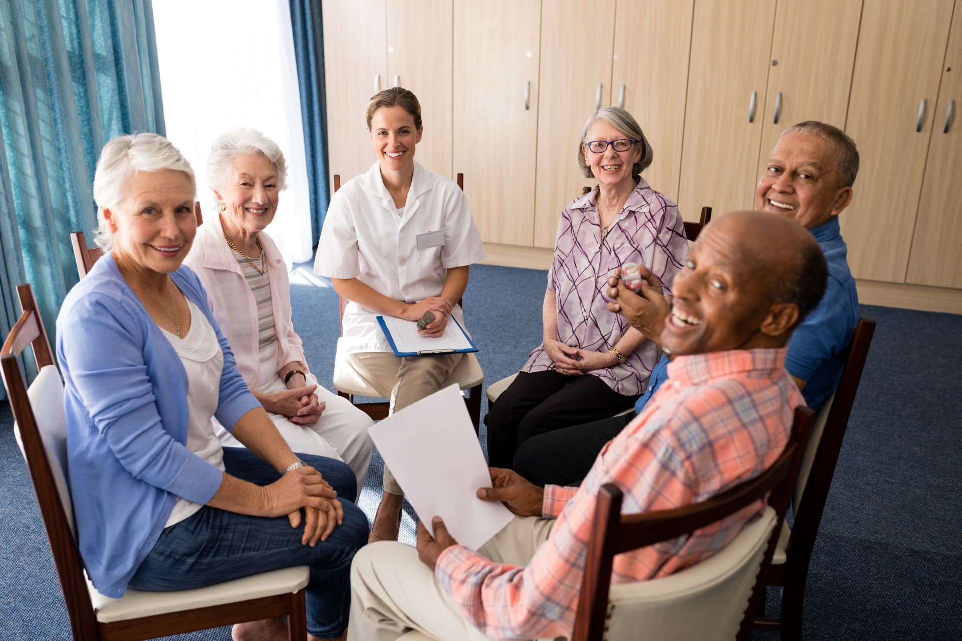 A group of elderly people are sitting in a circle with a nurse.