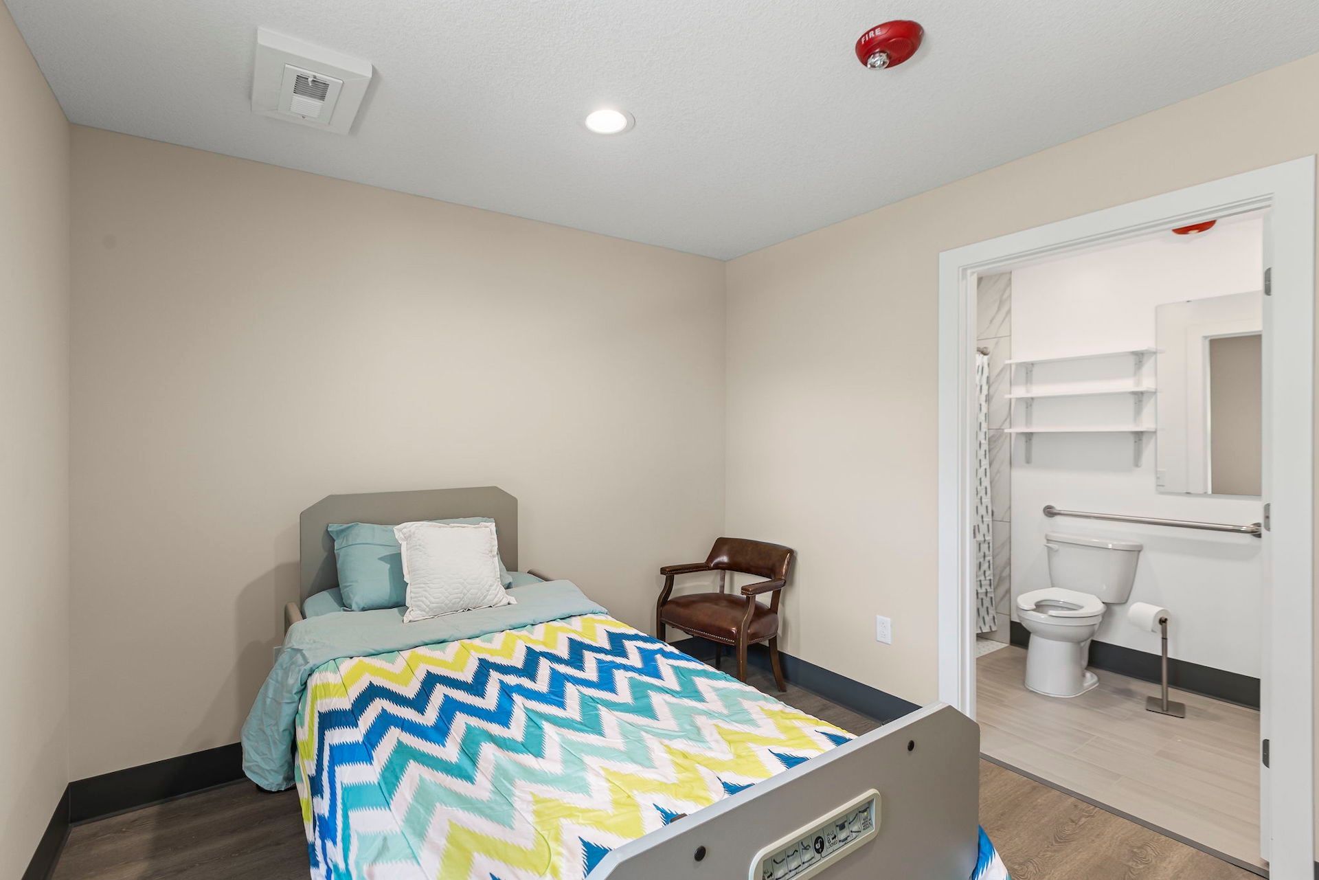 A bedroom with a bed , chair , toilet and bathroom.