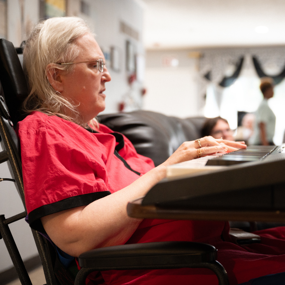 Woman in a wheelchair playing a keyboard, wearing a red shirt. Indoors.