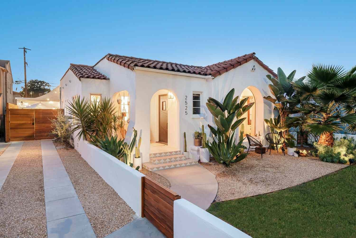 White stucco Spanish-style house with arched entryways, brown roof, and lush landscaping.