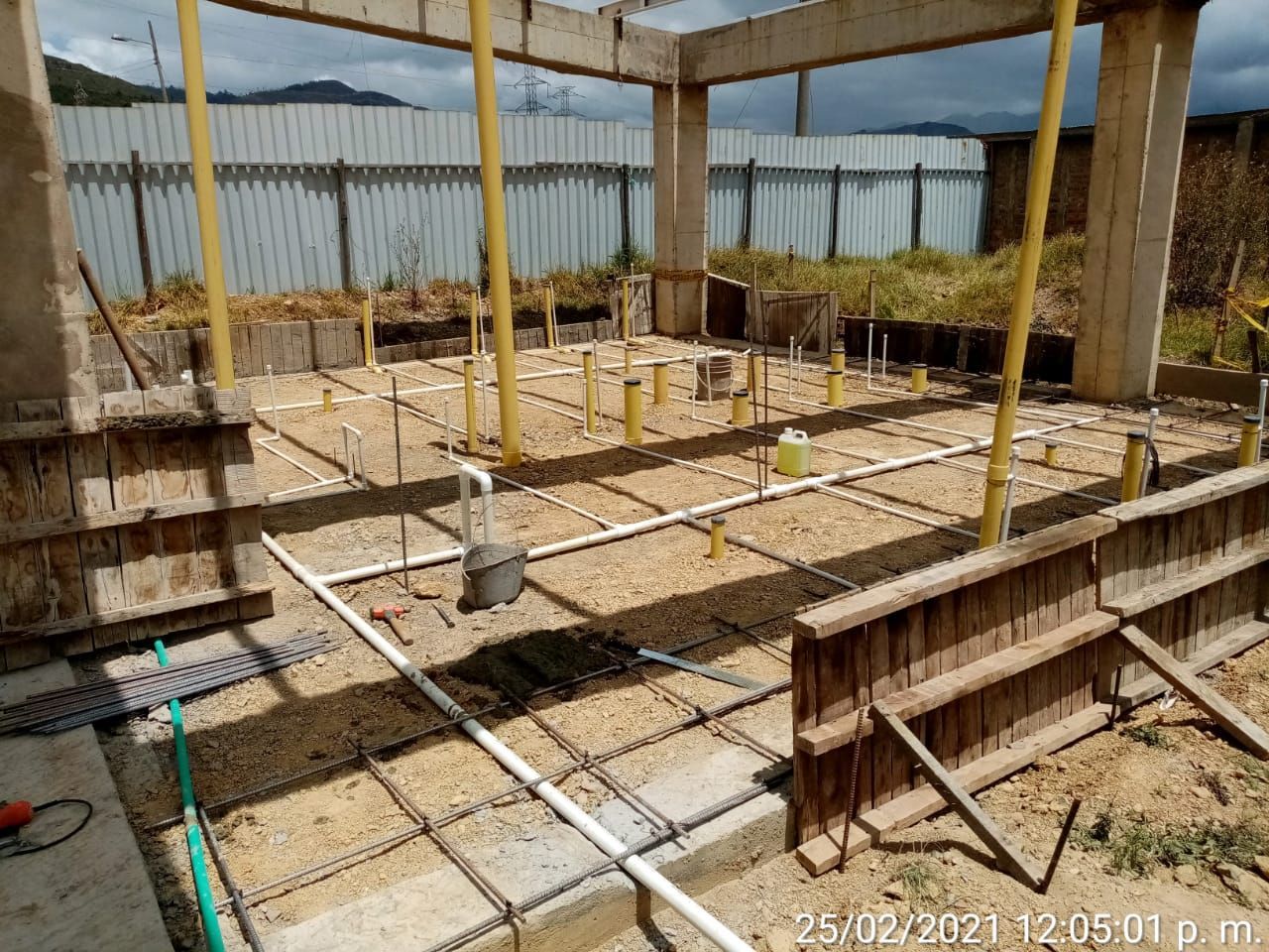 Obra con cimientos de hormigón y grifería. Estructura parcialmente construida con varillas y tuberías expuestas.