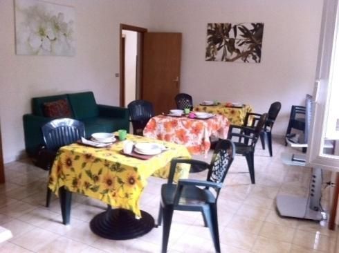 Soggiorno con tre tavoli apparecchiati per i pasti, divano e quadri alle pareti.