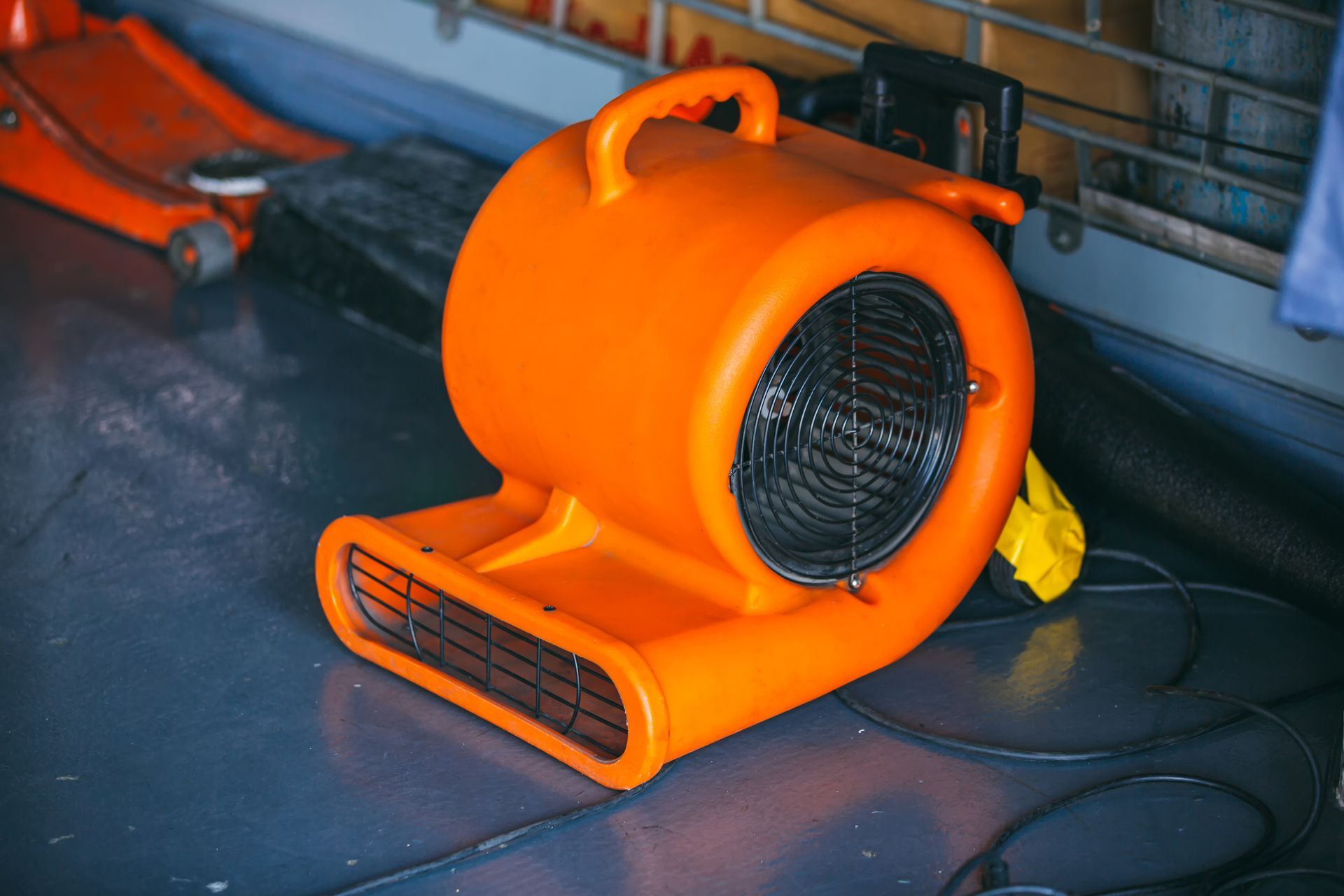 A bright orange air mover fan sits on a dark gray floor.