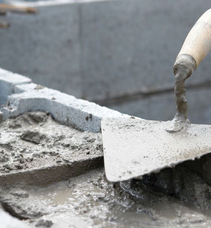 A person is using a trowel to spread concrete on a brick wall.