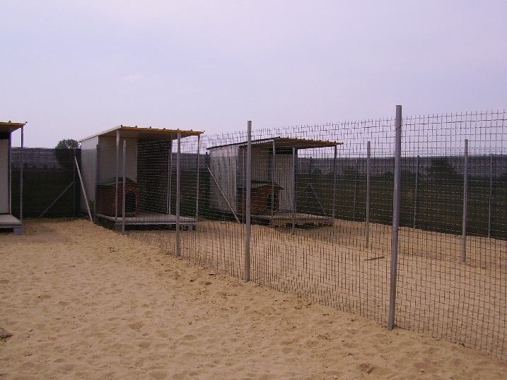 Una recinzione circonda un'area sabbiosa con alcuni edifici sullo sfondo.