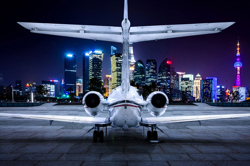 A private jet is parked on a runway in front of a city skyline at night.