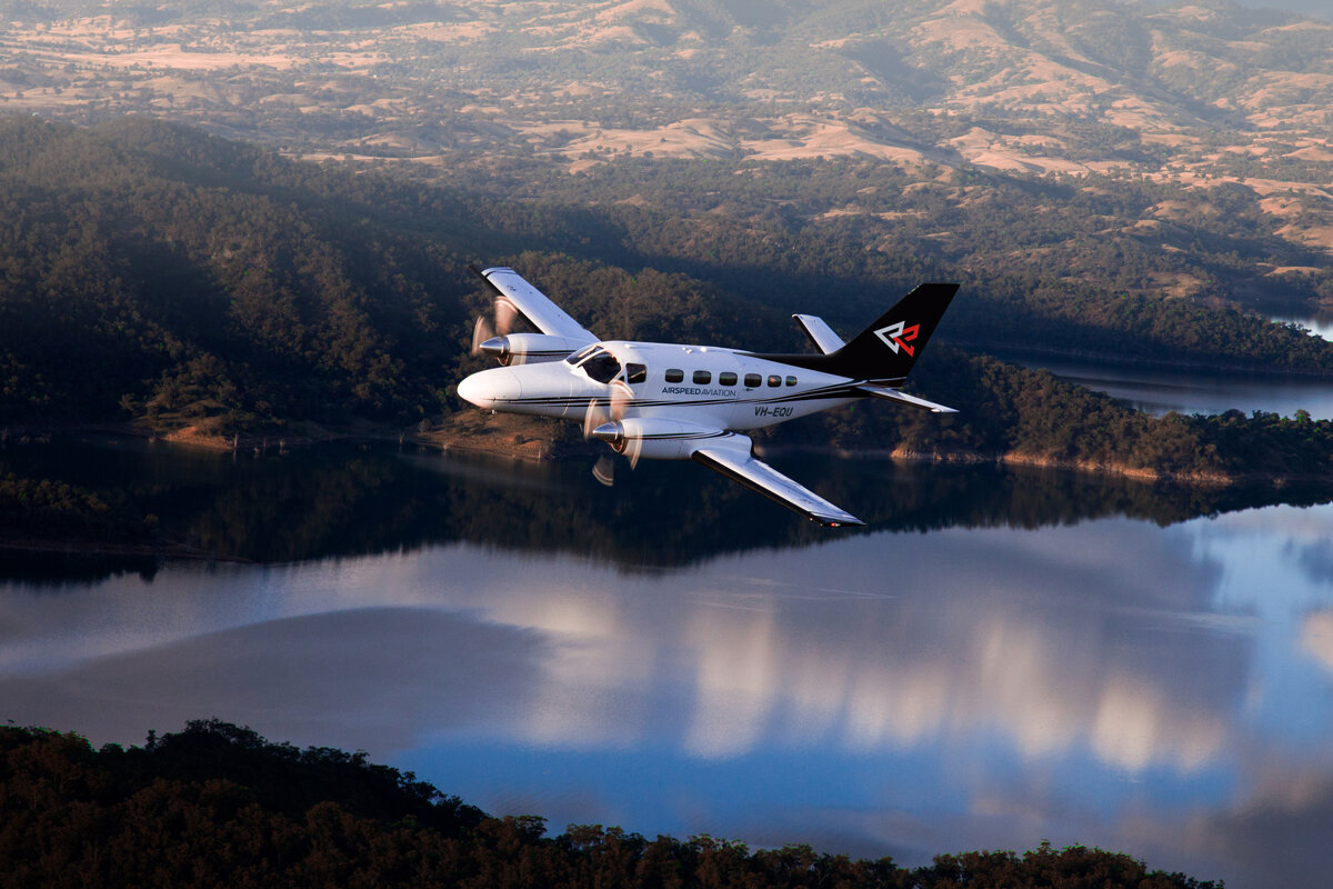 A small propeller plane is flying over a lake.