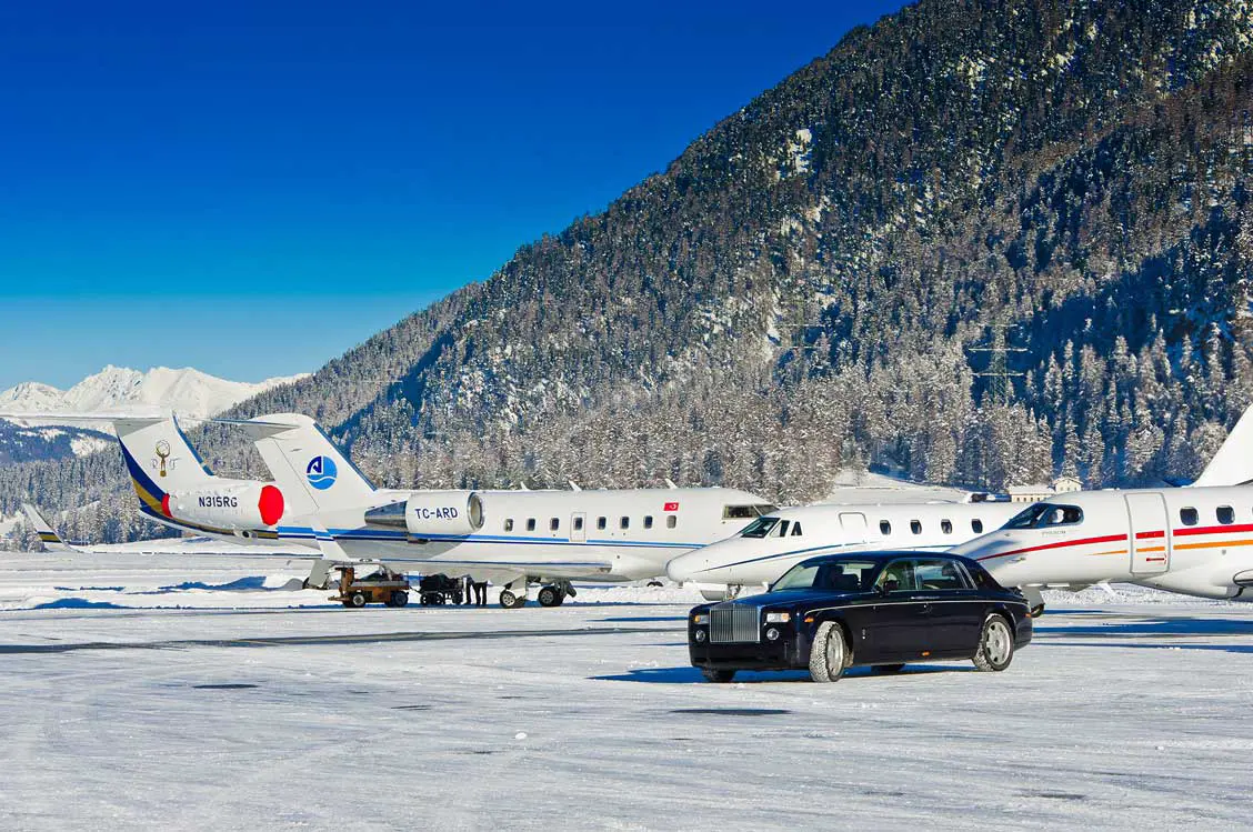 A car is parked in front of a row of planes on a snowy runway.