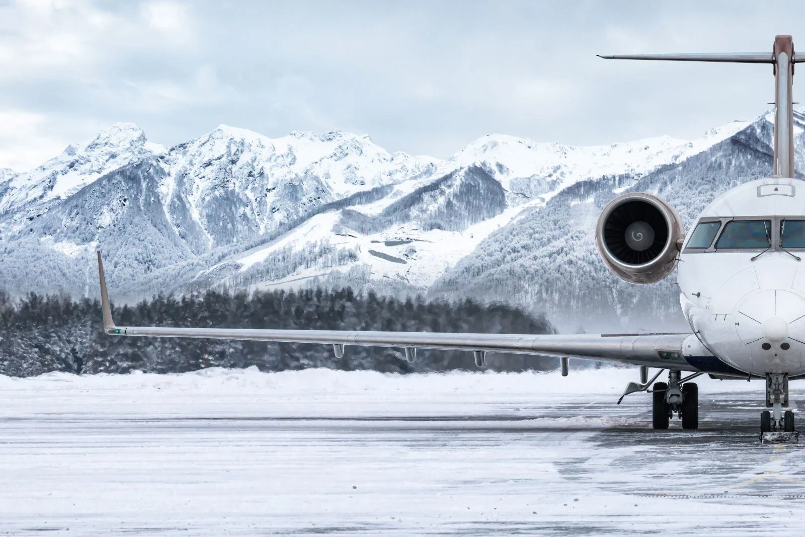 A private jet is parked on a snowy runway in front of snow covered mountains.