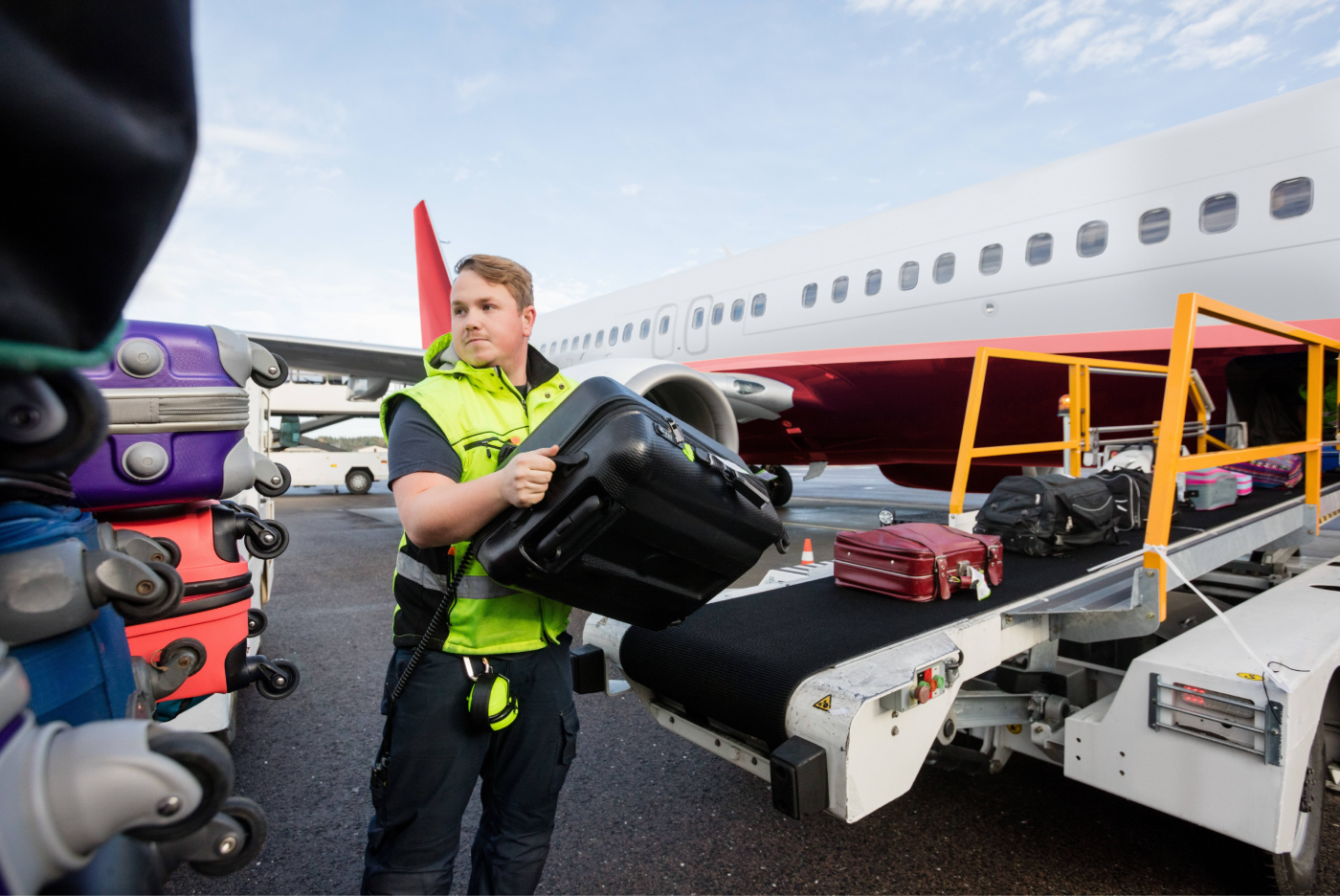 A man is carrying a suitcase on a conveyor belt in front of an airplane.