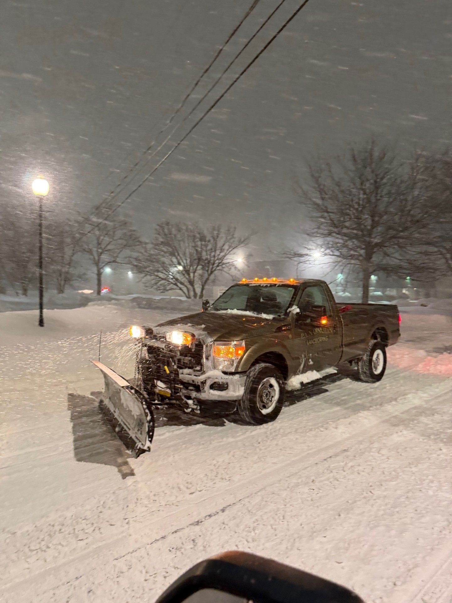 A row of several pickup trucks equipped with yellow snowplows parked on a snow-covered lot in front of a garage.