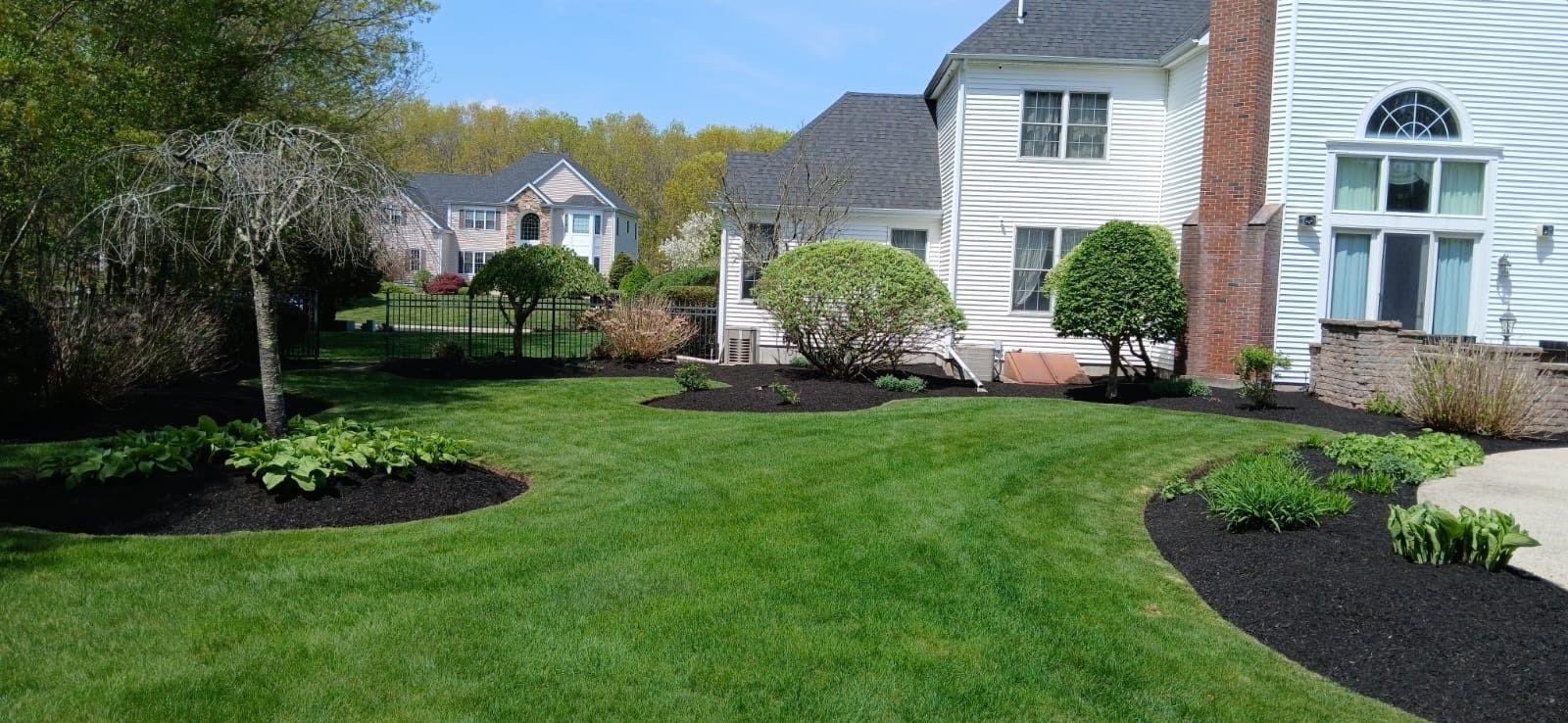 A person gardens in front of a two-story light gray house with a white porch and an attached garage.