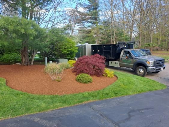 A dump truck parked on a driveway next to a landscaped garden bed with fresh brown mulch and various shrubs.