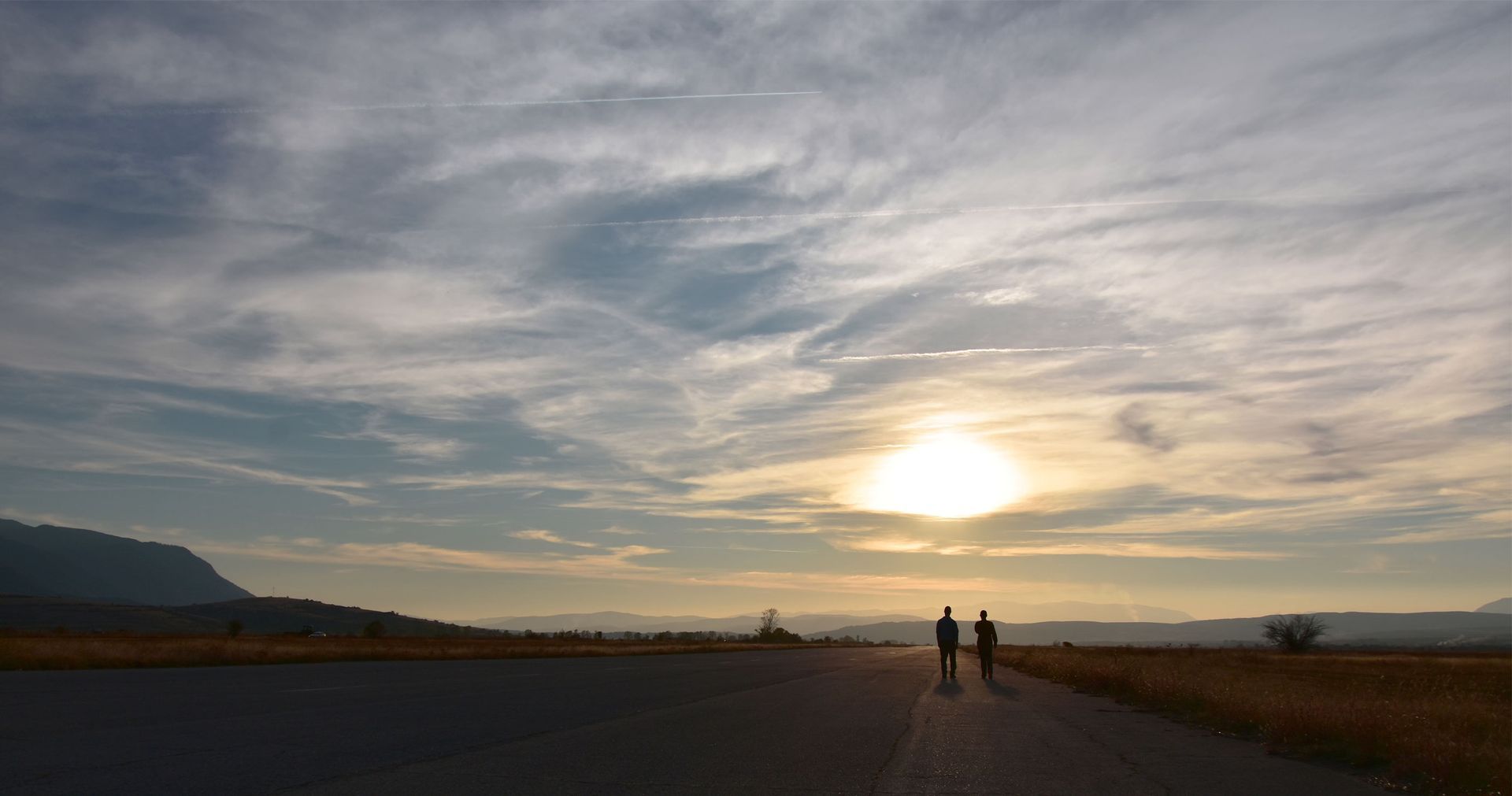 Two people are walking down a road at sunset.