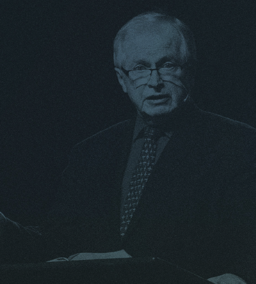 A man in a suit and tie is giving a speech in a dark room.