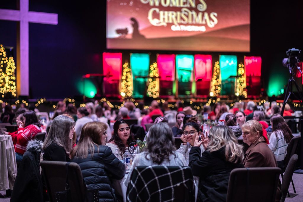 A group of people are sitting at tables at a women 's christmas dinner.