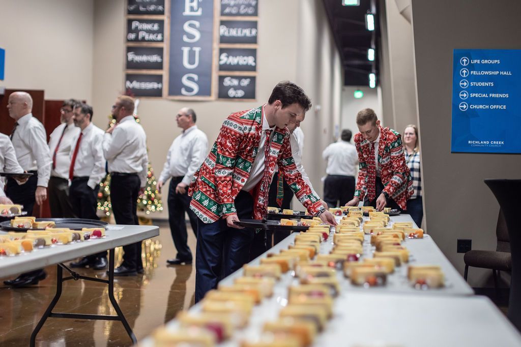 A group of men are standing around a long table filled with food.