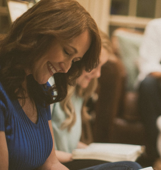 A woman in a blue shirt is smiling while reading a book