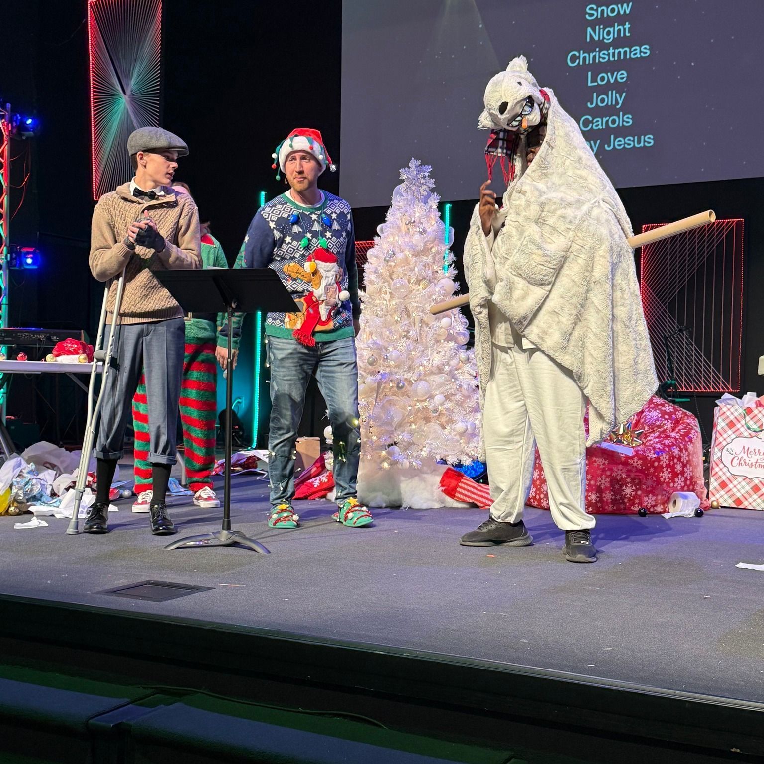 A group of people are standing on a stage with christmas trees in the background.