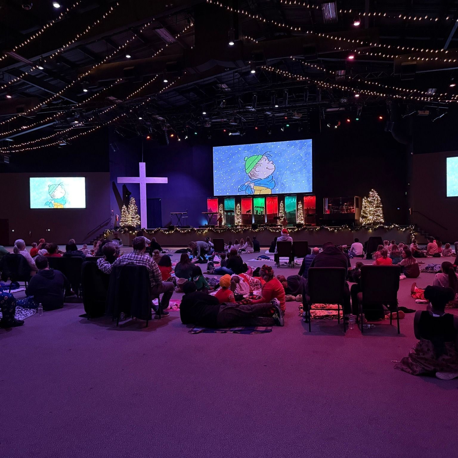 A large group of people are sitting in a large room with a large screen on the stage.