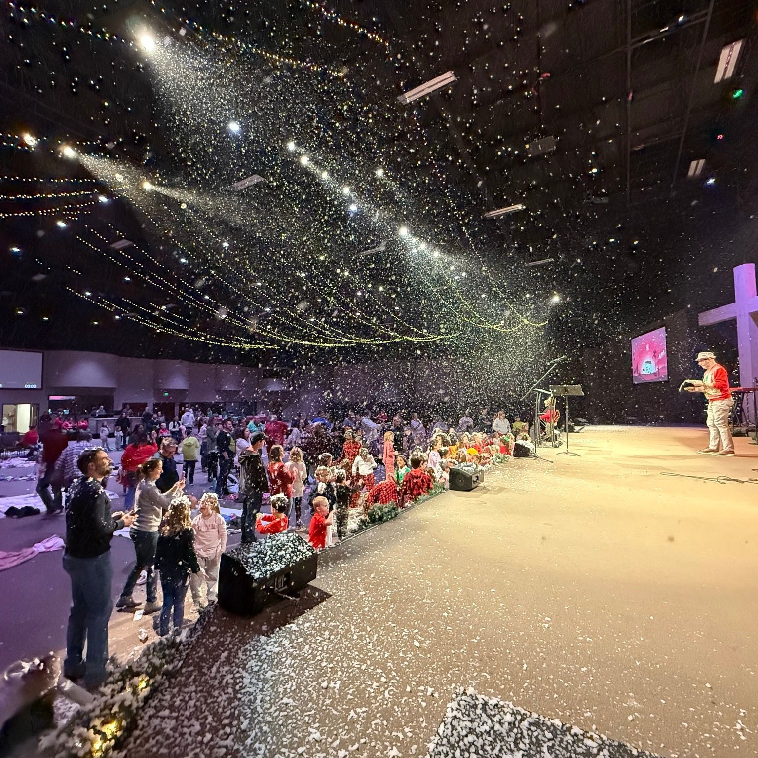 A large group of people are standing in a large room with confetti falling from the ceiling.