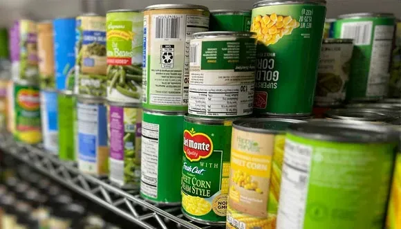 A shelf filled with cans of food including corn and green beans.