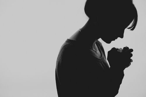 A silhouette of a woman praying with her hands folded.