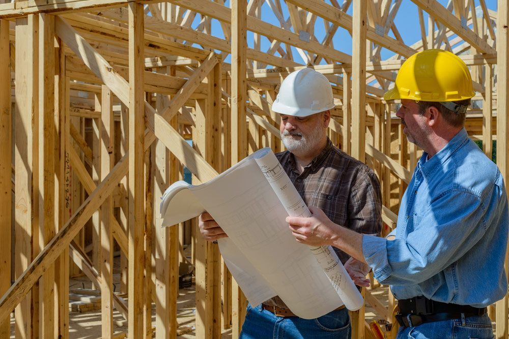 Two Men Looking At Plans On The Construction Site With The Frame Timber House In The Background — Trussted Frames & Trusses in Cessnock, NSW