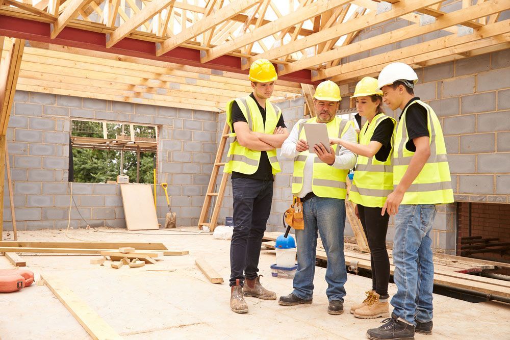 Four Builder Looking On The Blueprint With Wooden Framing House — Trussted Frames & Trusses in Cessnock, NSW