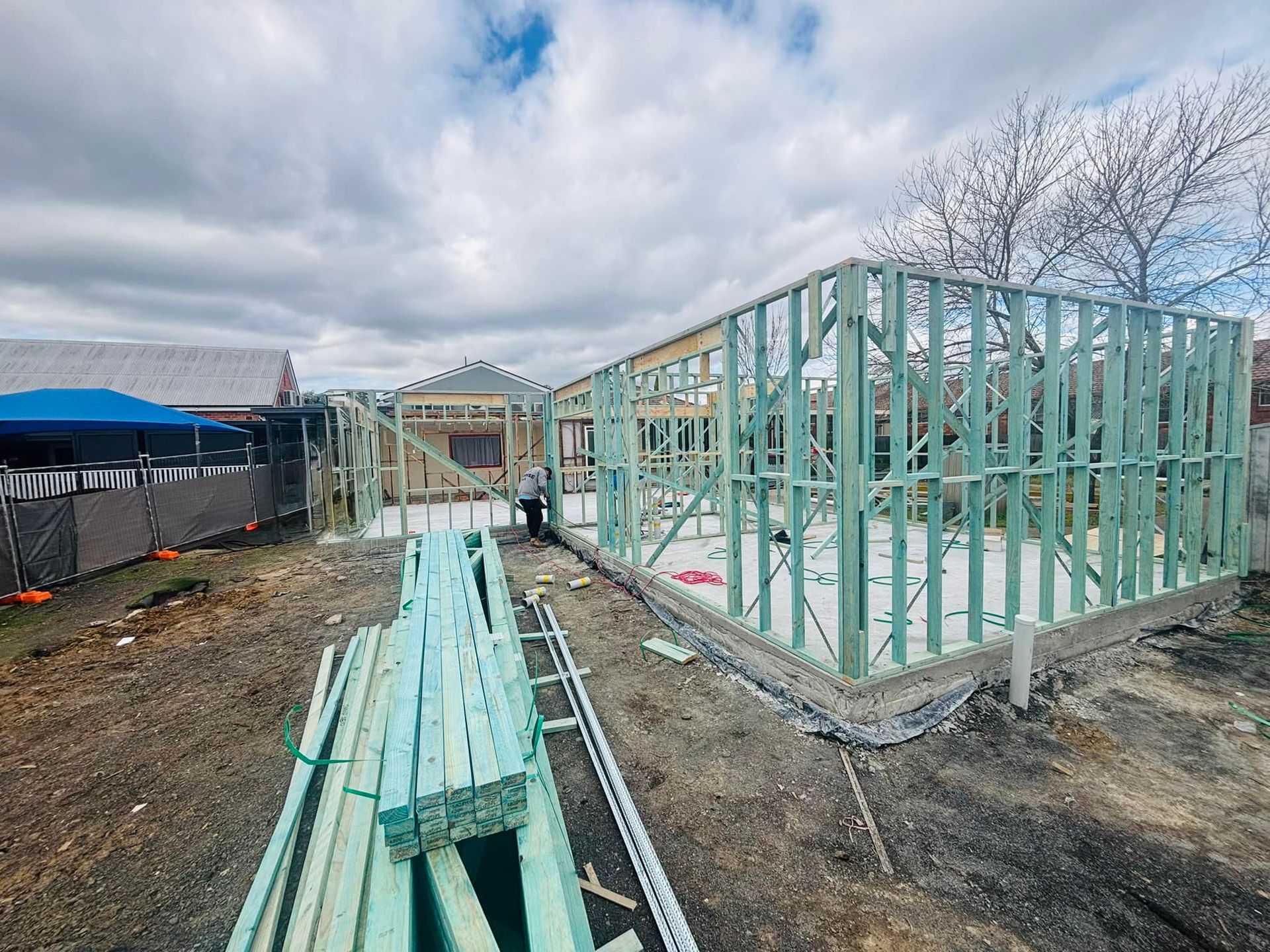 Construction Site With Wooden Frame Walls on a Concrete Foundation, Lumber Piles in Foreground — Trussted Frames & Trusses in Bennetts Green, NSW