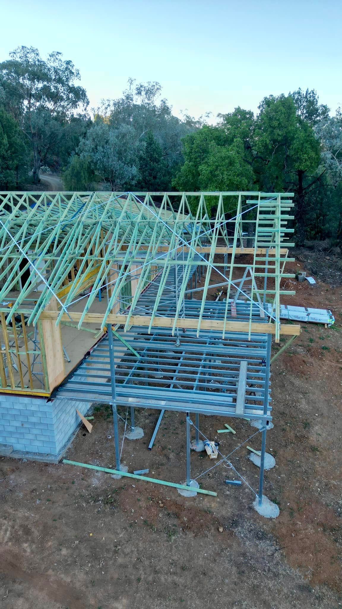 Construction Site, Partially Built House Frame With Wooden Beams and Supports, Set in a Natural Landscape With Trees and Dirt — Trussted Frames & Trusses in Bennetts Green, NSW