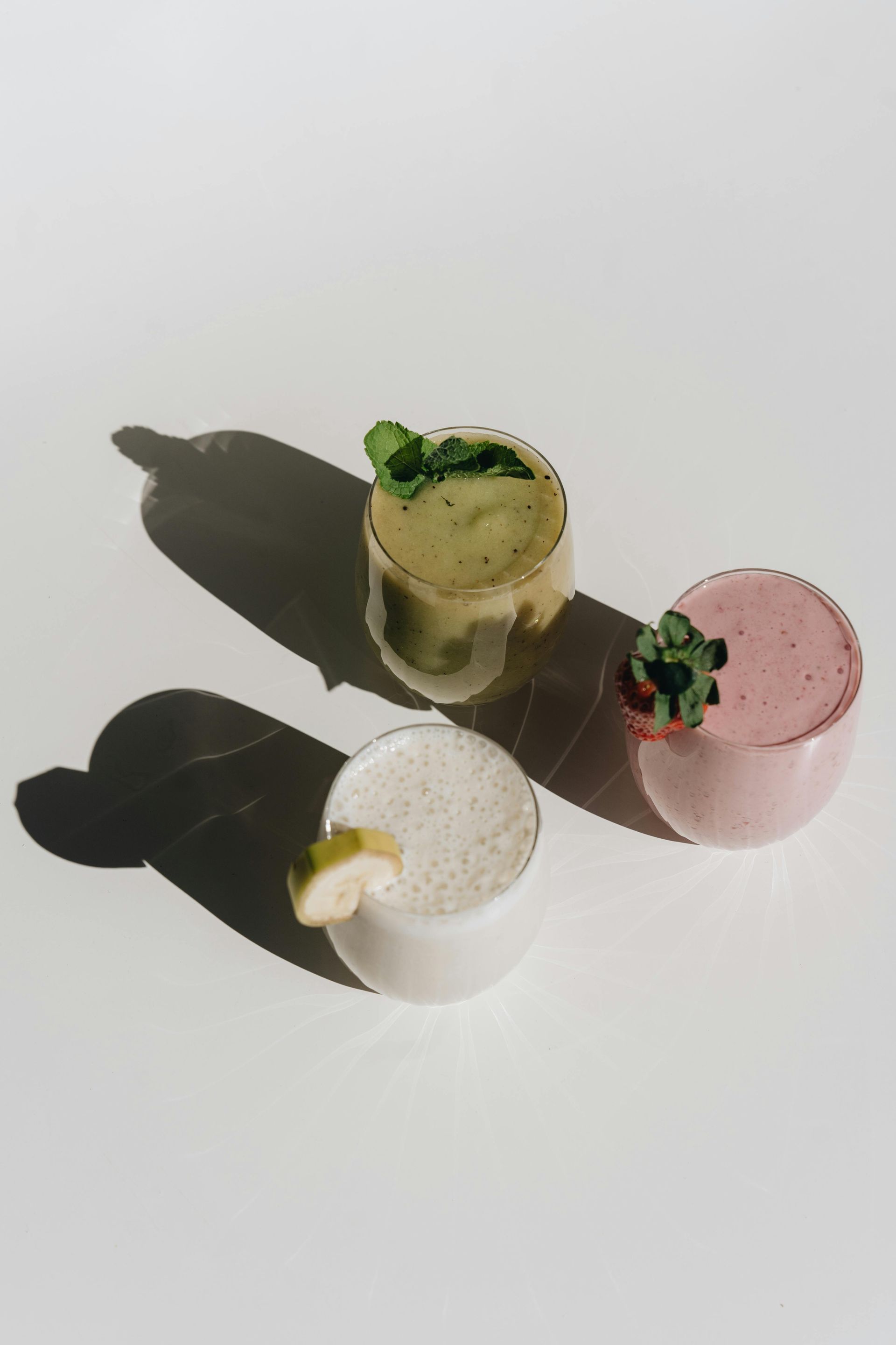 Three small dessert cups with green, pink, and white toppings on a white surface.