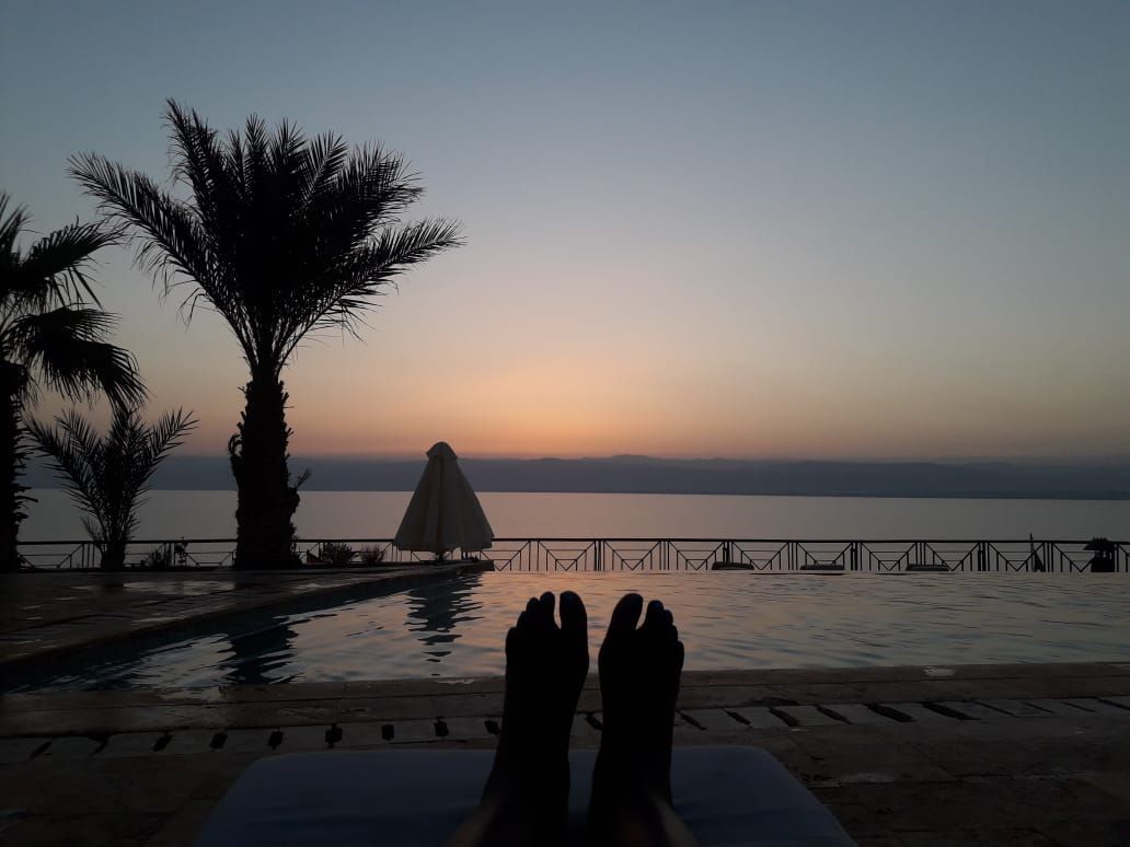 Felicia's feet are resting on a chair near a swimming pool at sunset