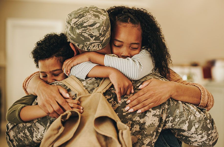 a man in a military uniform is hugging his wife and two children .