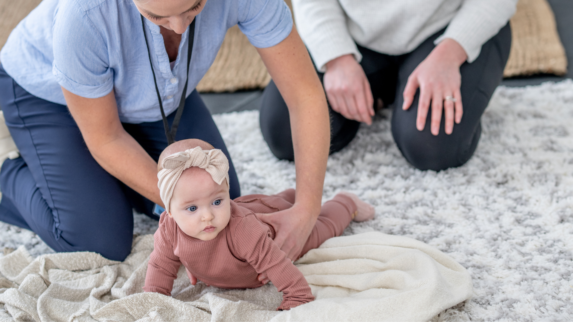 Two women are kneeling down next to a baby on the floor.