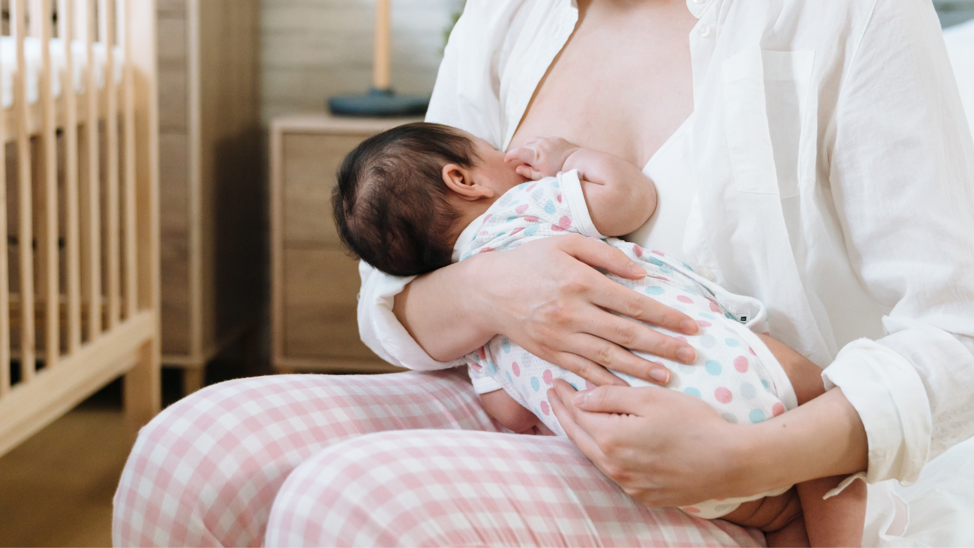 A woman is breastfeeding her baby while sitting on a bed.