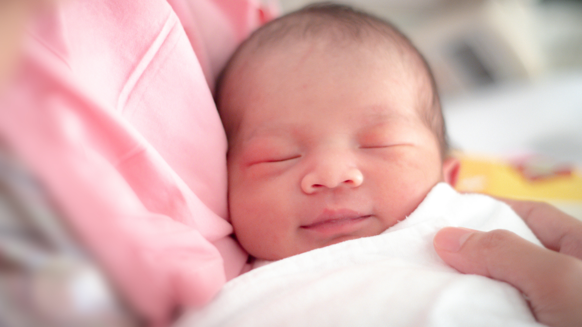 A woman is holding a newborn baby wrapped in a pink blanket.