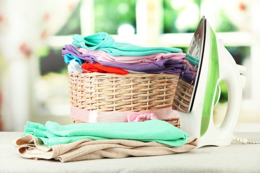 Steam iron and wicker basket with clothes, on bright background