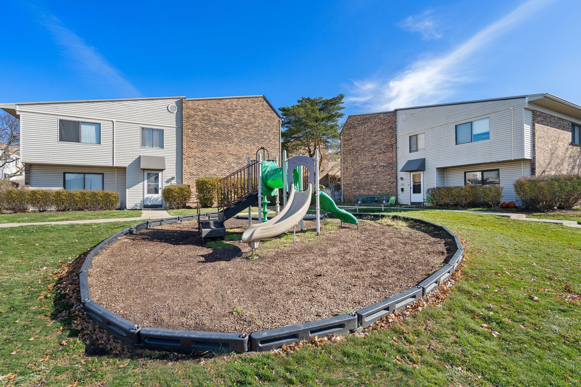 Apartment courtyard playground with green play structure and mulch bed between two buildings