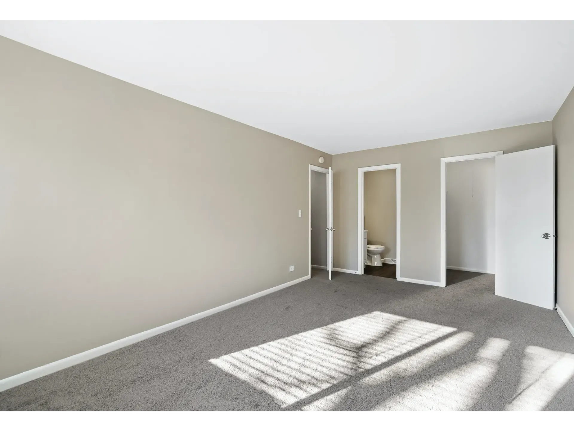 Interior view of a vacant apartment room with light carpet and neutral walls